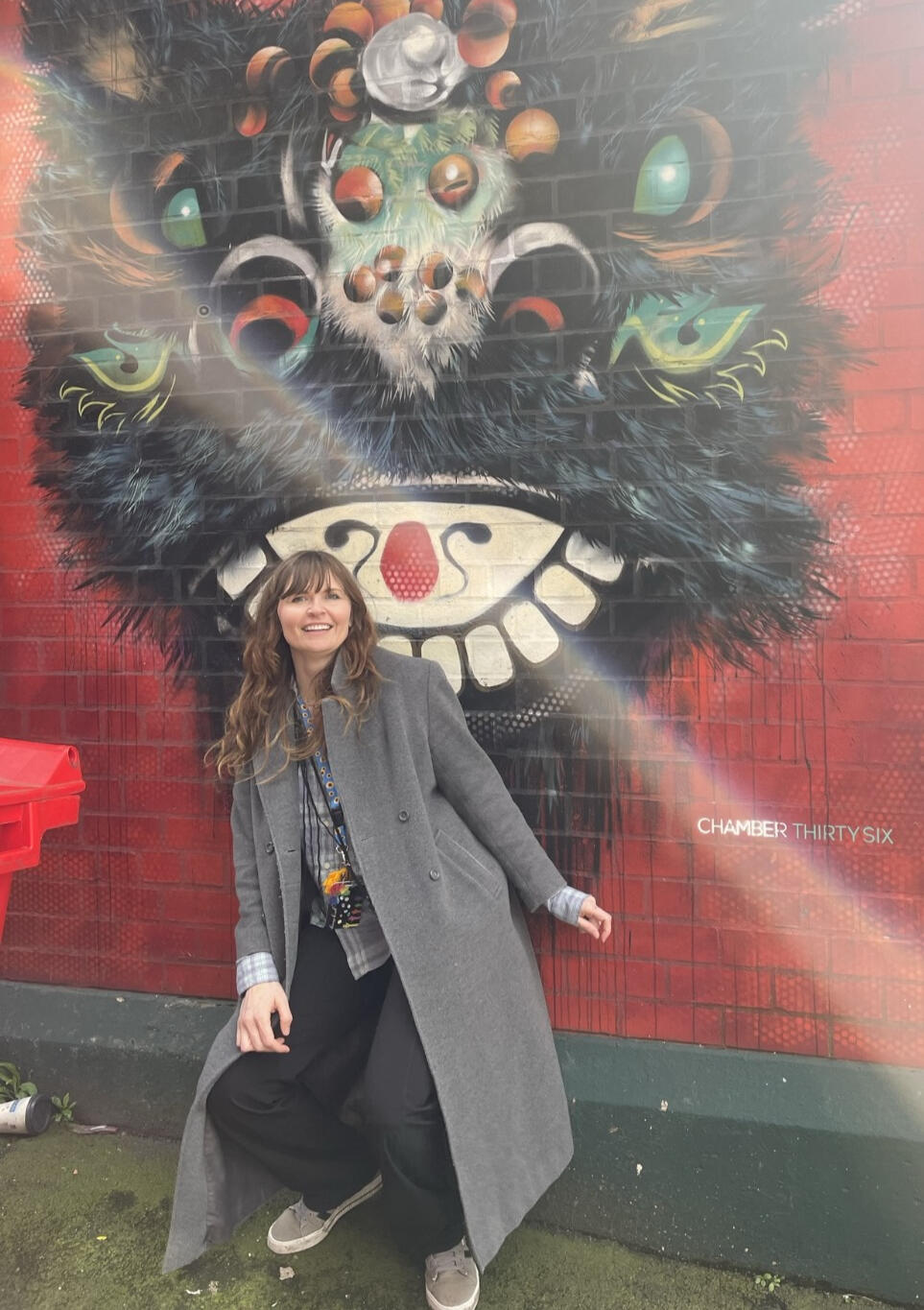 Woman leaning up against an elaborate mural painted on a brick wall in Liverpool
